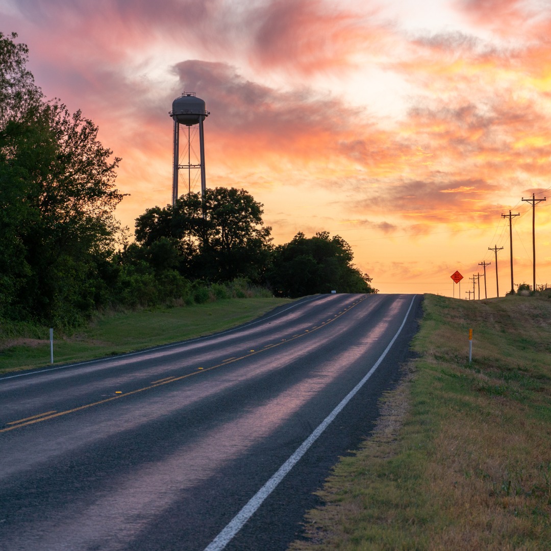 An orange sunset lights up a country road and a nearby water tower – a metaphor for the coming darkness in rural healthcare